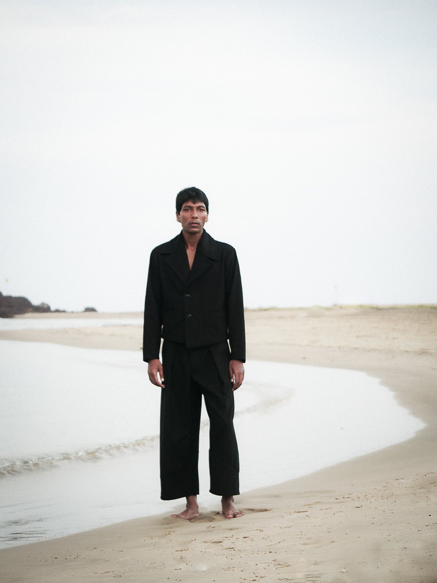 Person wearing a black outfit standing on a beach with a minimal background