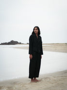 Person wearing a black outfit standing on a beach with a minimalistic background