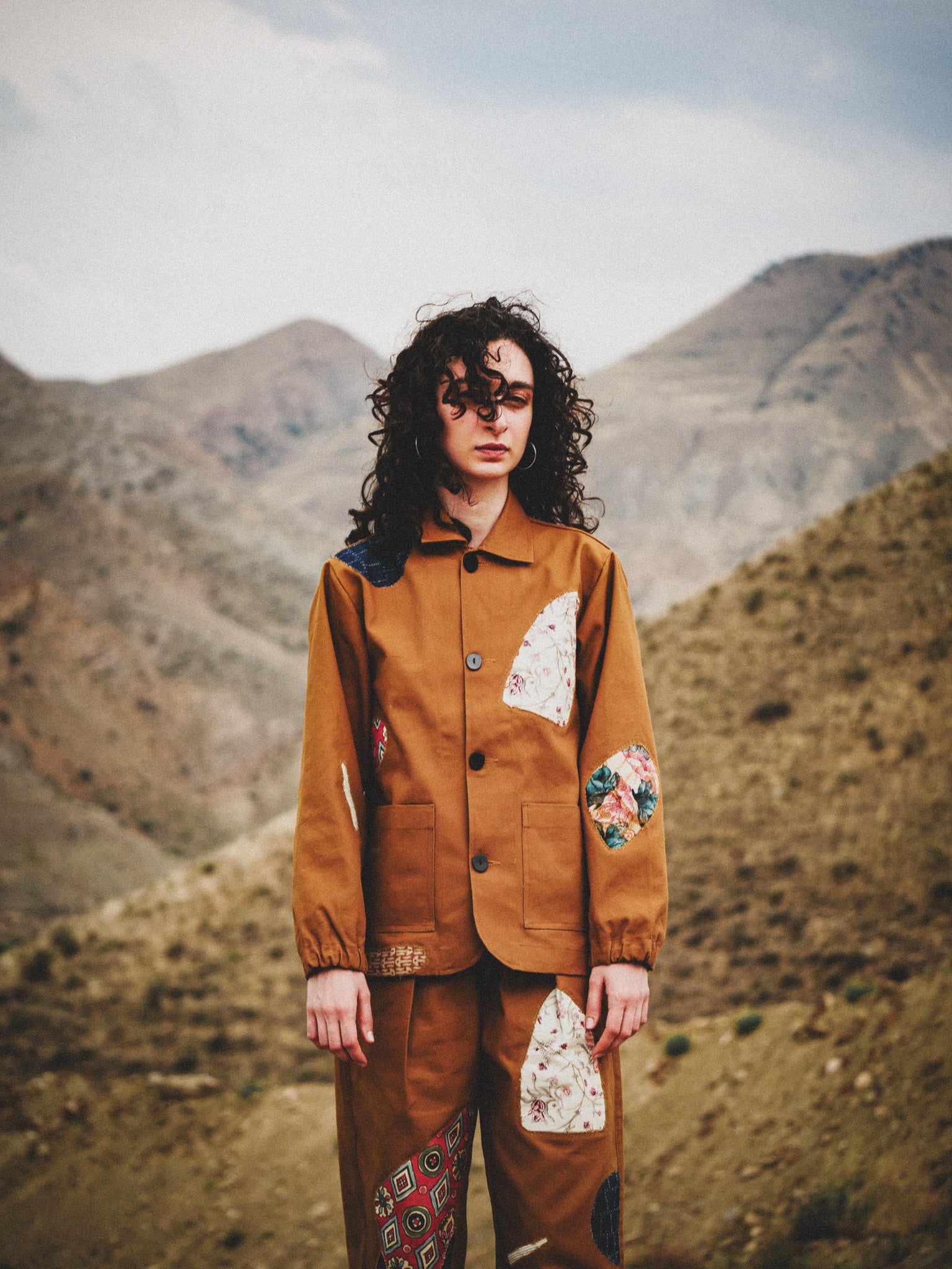 Person wearing a brown jacket with floral designs in a mountainous landscape