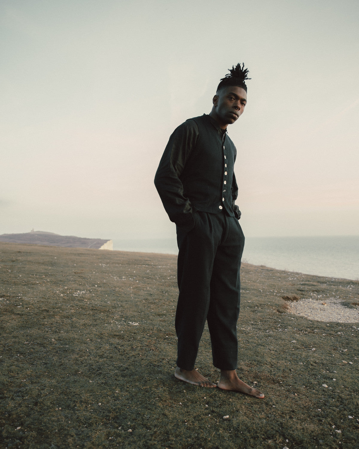 Man standing on a grassy field in black trousers and waistcoat with a plain background