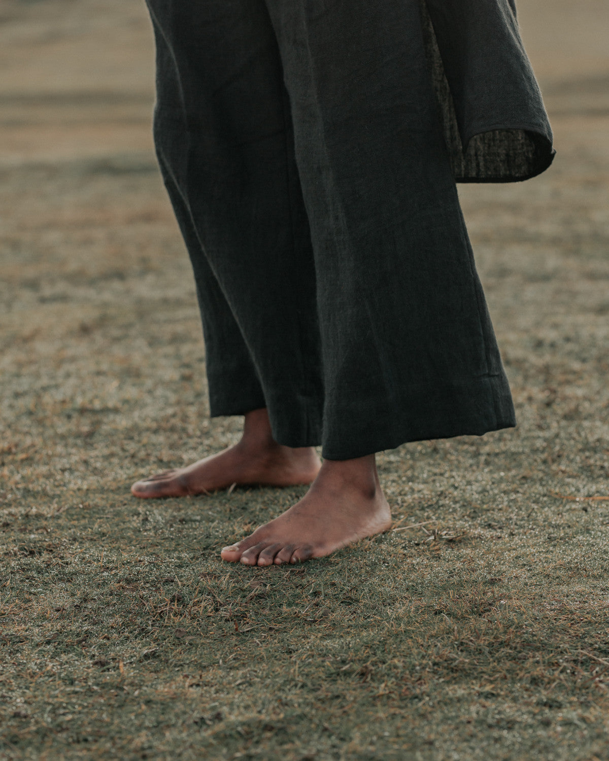 Person wearing black wide legged trousers standing on a grassy field