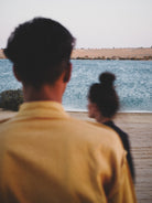 Two people standing by a body of water, looking out towards the horizon.