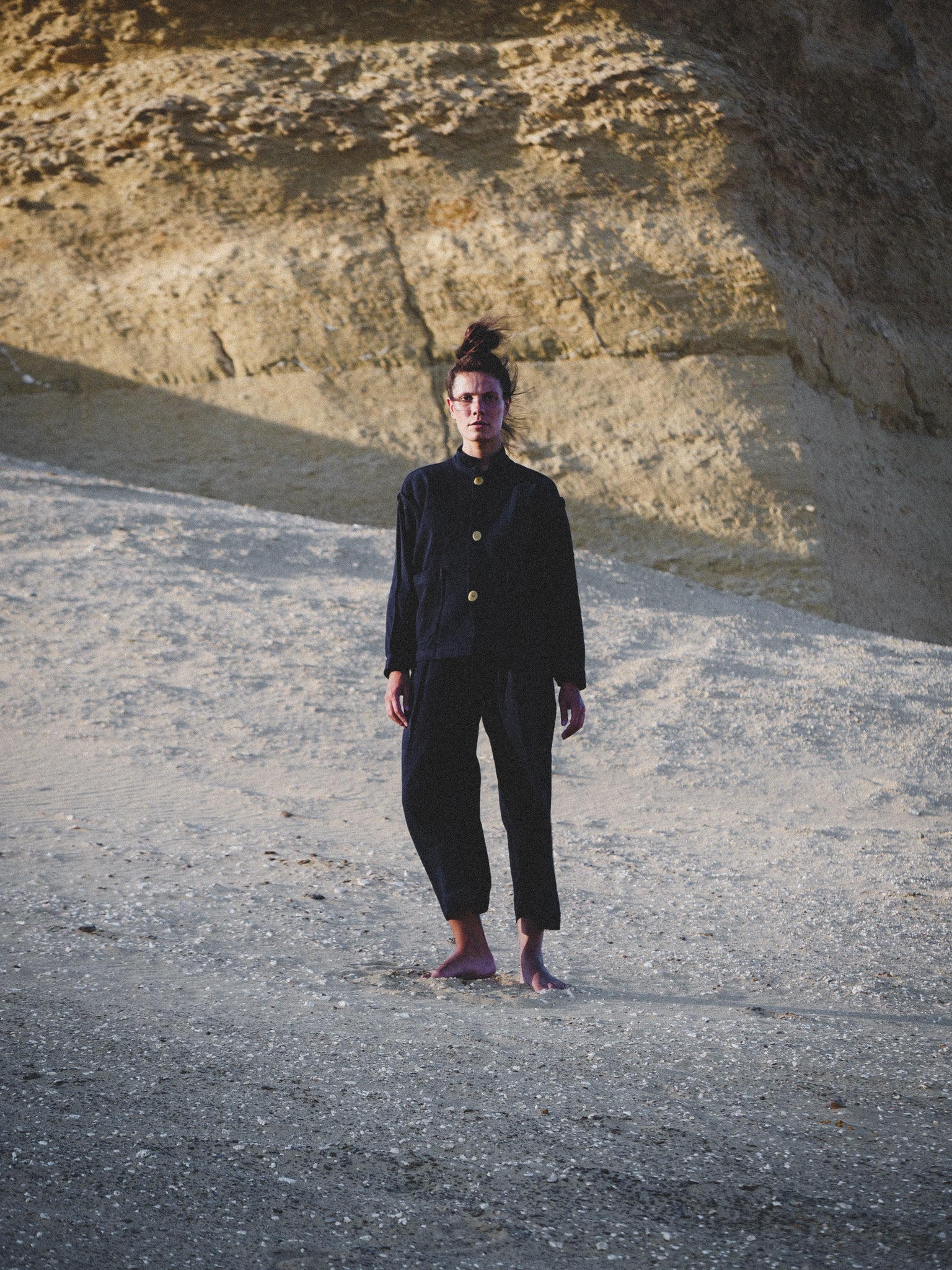 Person wearing a navy outfit standing on a rocky surface with a natural rock formation in the background