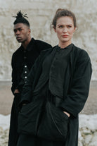 Two people wearing black outfits standing against a textured wall.
