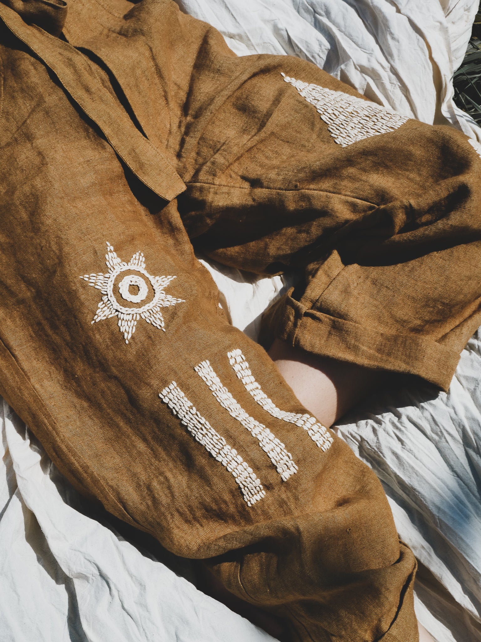 Brown trousers with white embroidery on a textured surface