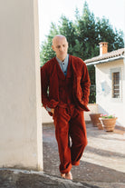 Man in a red corduroy suit standing outdoors near a building with trees in the background