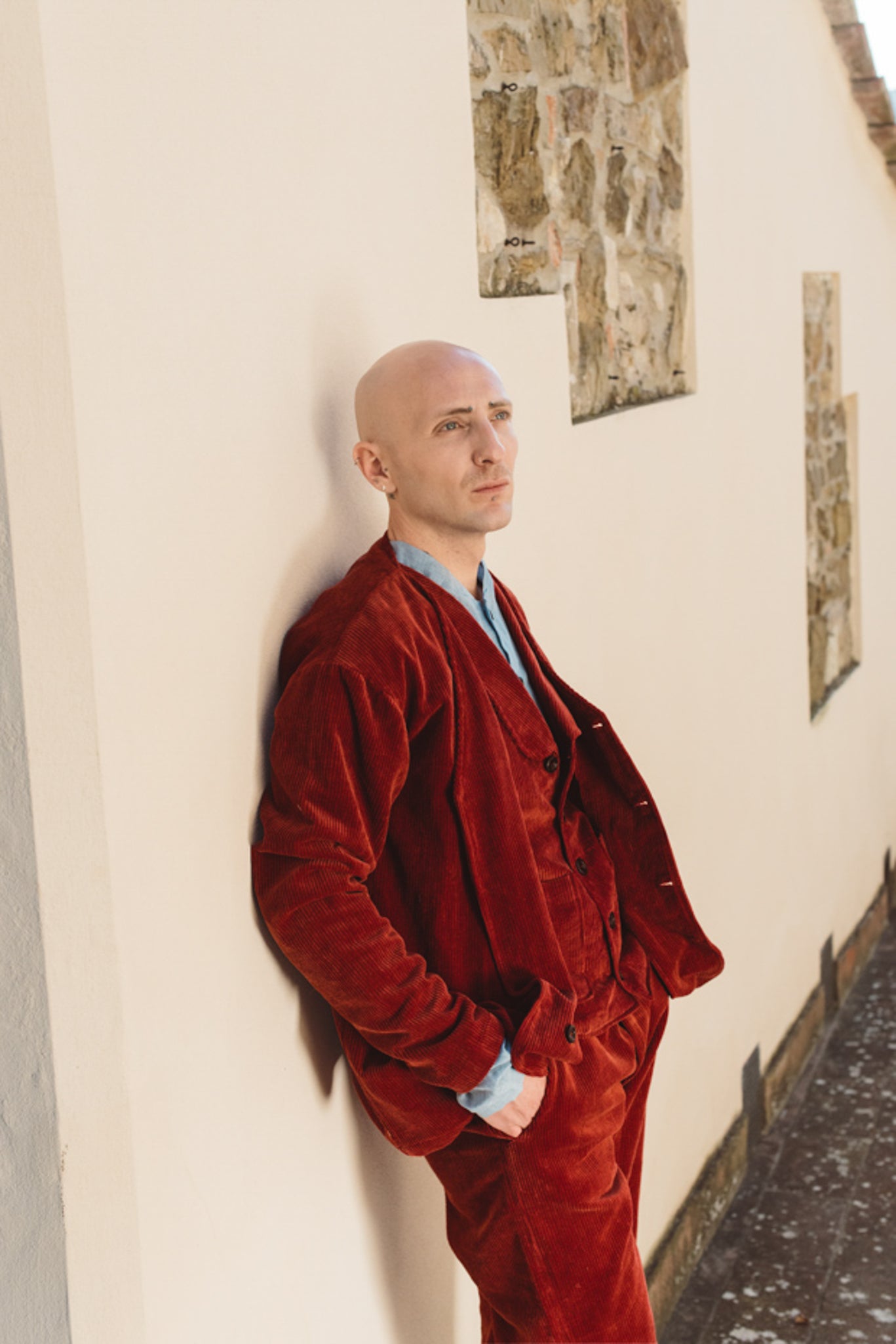 Man in a red corduroy outfit standing against a wall with framed pictures.