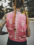 Person wearing a dark pink embroidered vest with braided hair in an outdoor setting