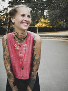 Woman with tattoos wearing a dark pink vest outdoors