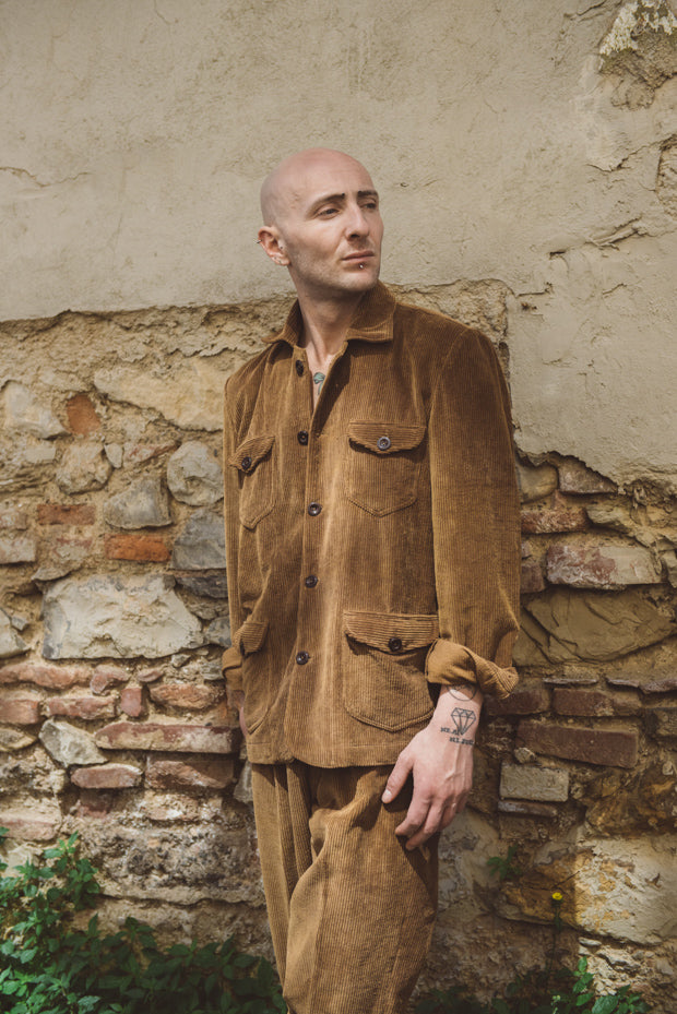 Man in a brown corduroy outfit standing against a stone wall.