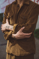 Person wearing a brown corduroy jacket with tattoos on arms