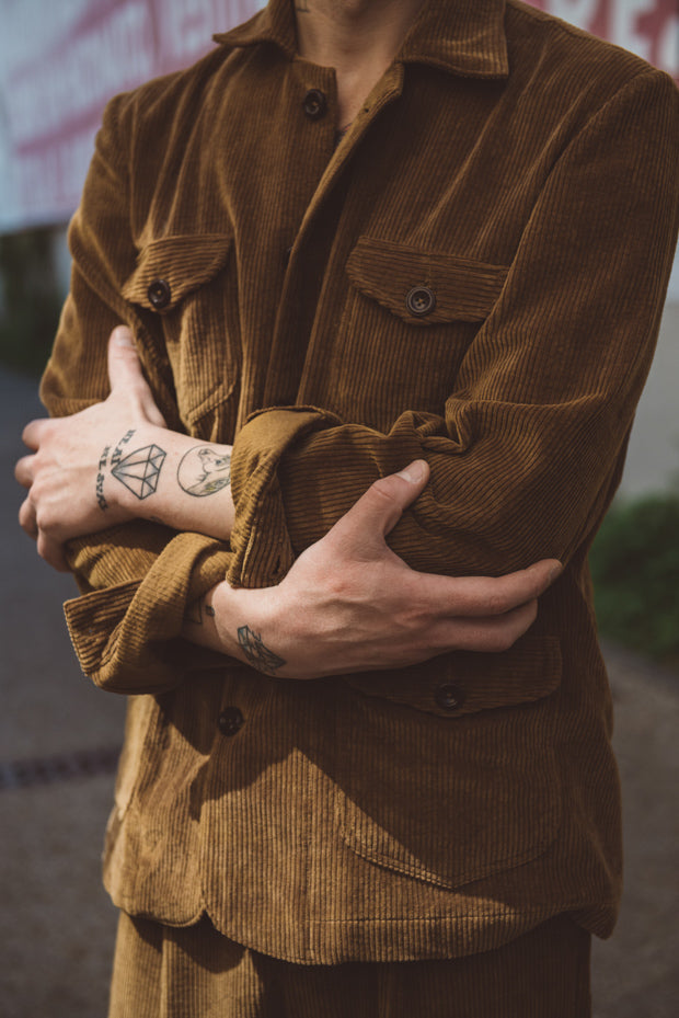 Person wearing a brown corduroy jacket with tattoos on arms