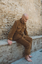 Man in brown corduroy outfit sitting against a stone wall.