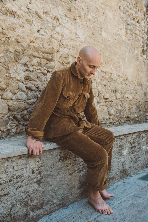 Man in brown corduroy outfit sitting against a stone wall.