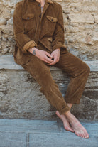 Person wearing a brown corduroy outfit sitting against a stone wall.