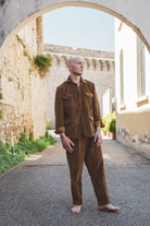 Man in a brown outfit standing in an alleyway with stone walls and plants.