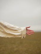 Beige sleeve of a garment with a hand reaching out against a neutral background