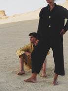 Two people in navy and yellow outfits standing on a sandy dune.