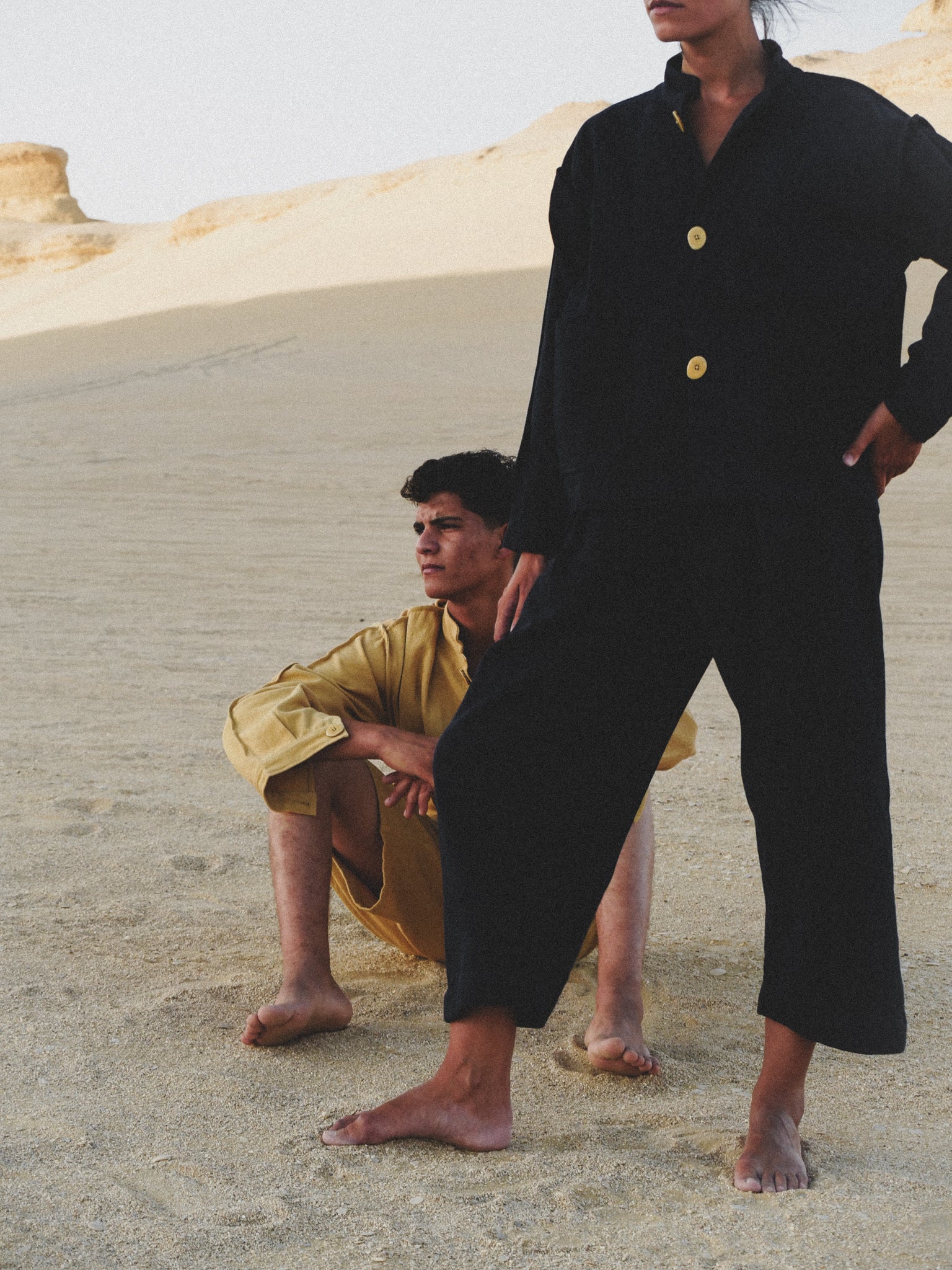 Two people in navy and yellow outfits standing on a sandy dune.