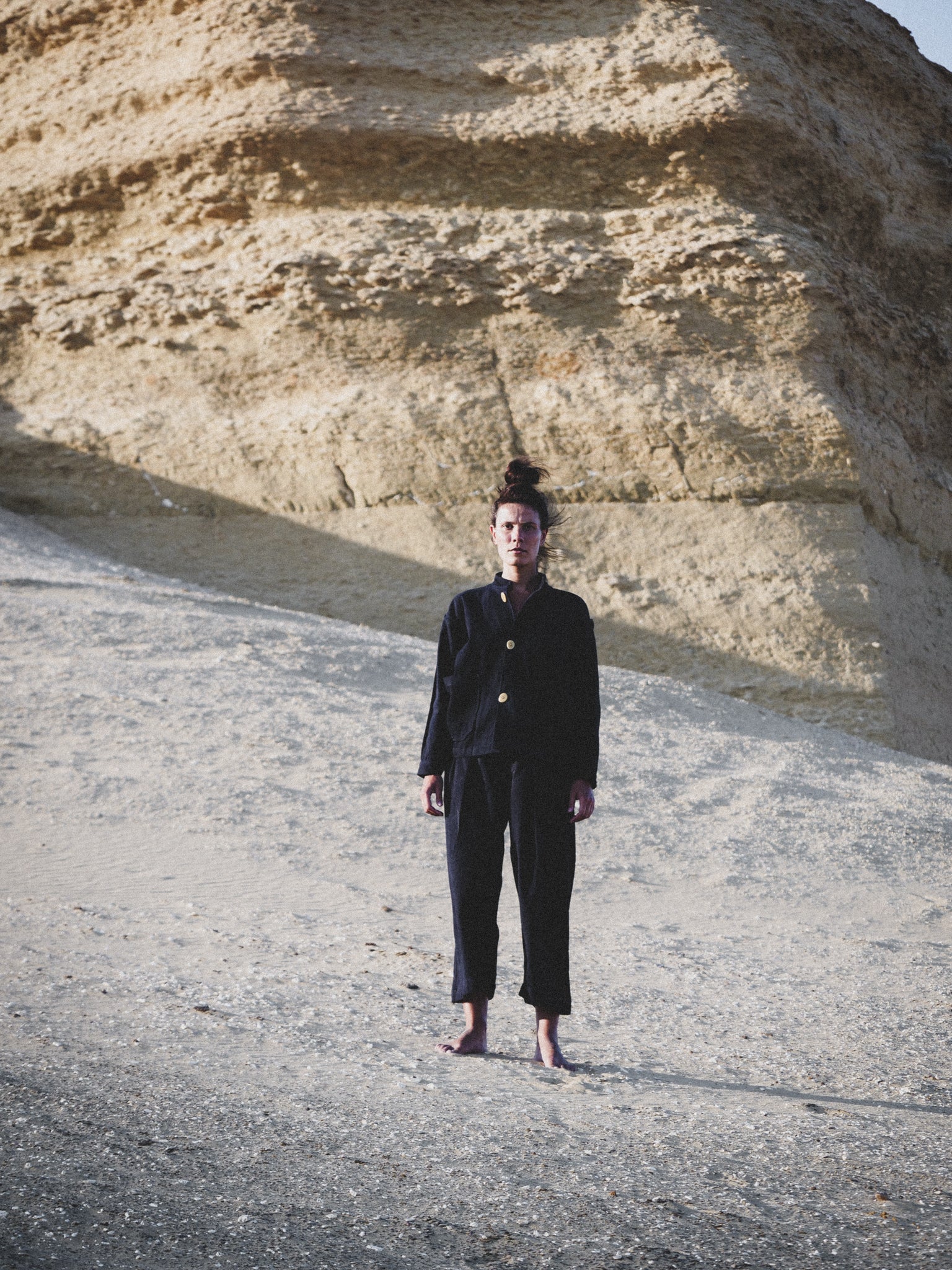 Person wearing a navy outfit standing in front of a rocky cliff.