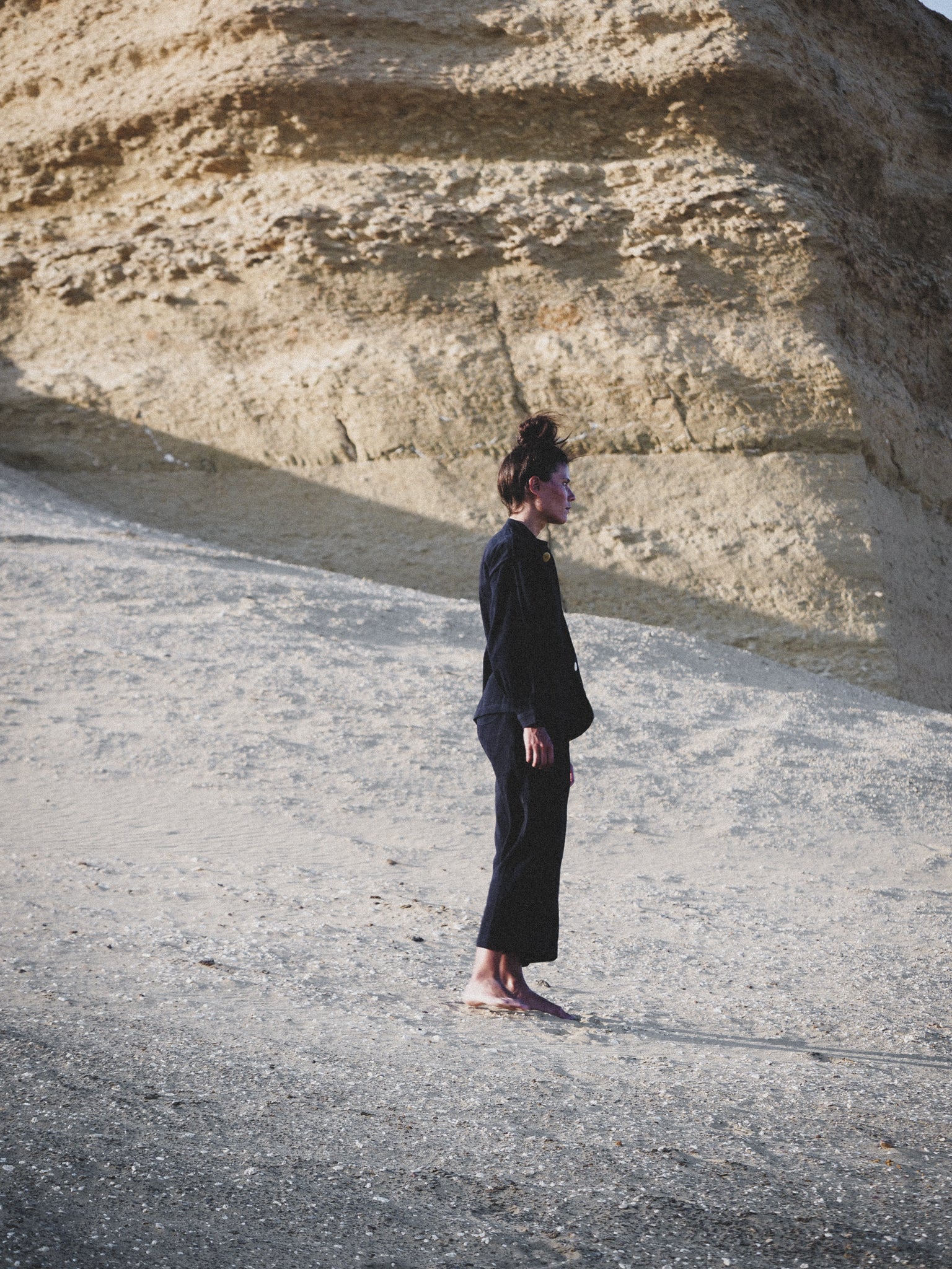 Person in navy outfit standing on a sandy beach with large rock formations in the background