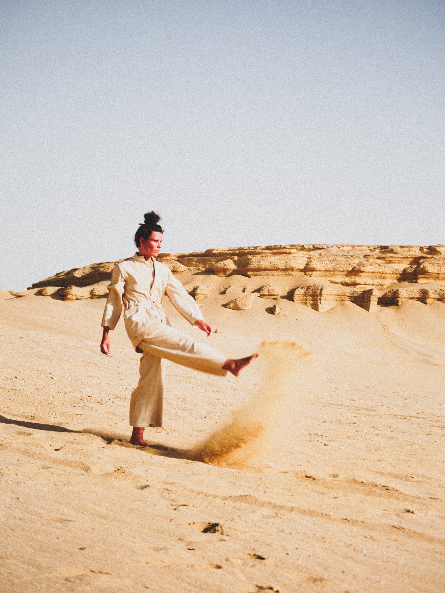 Person in a white outfit kicking up sand in a desert landscape