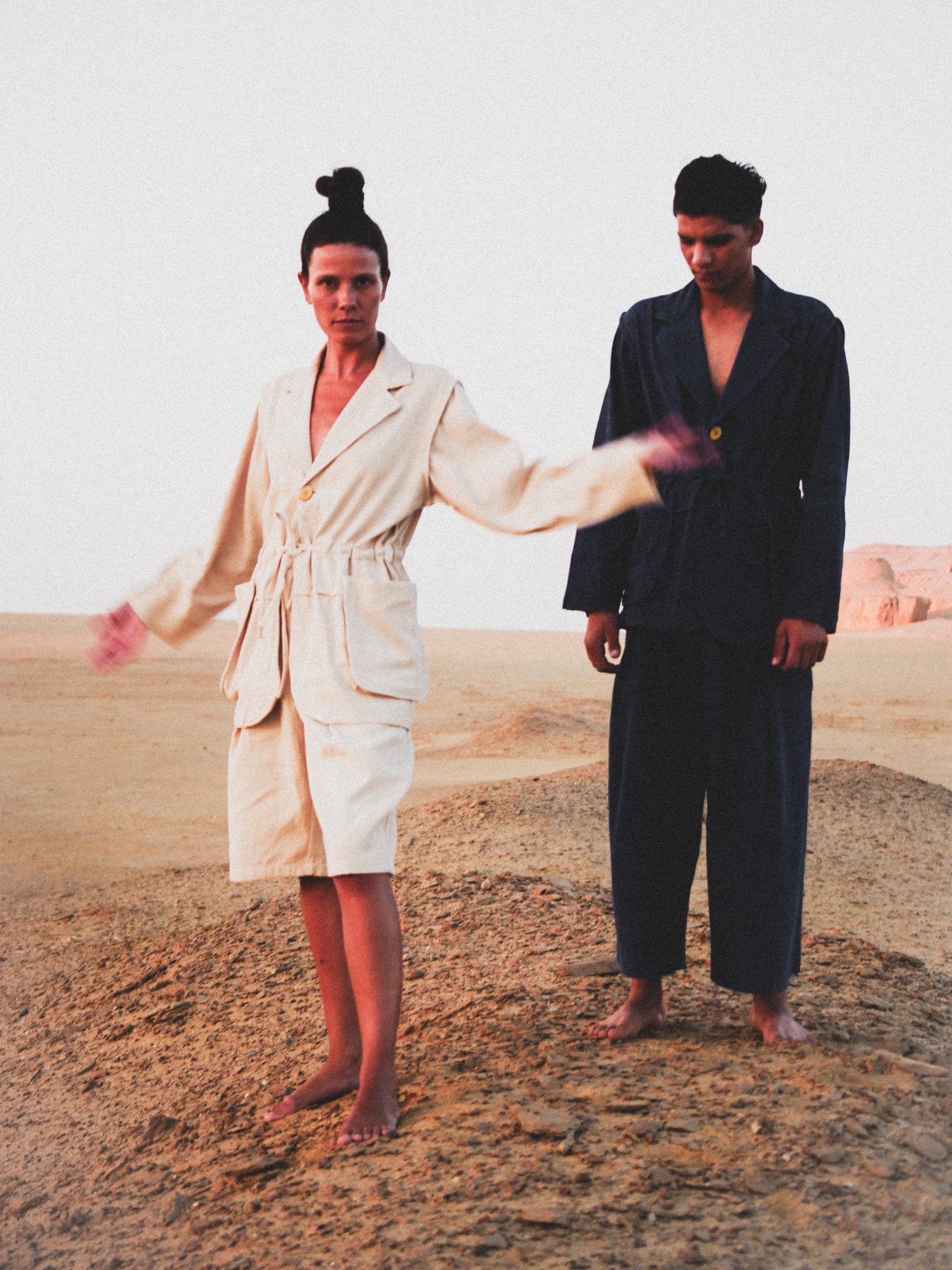 Two people in suits standing in a desert landscape with a plain background