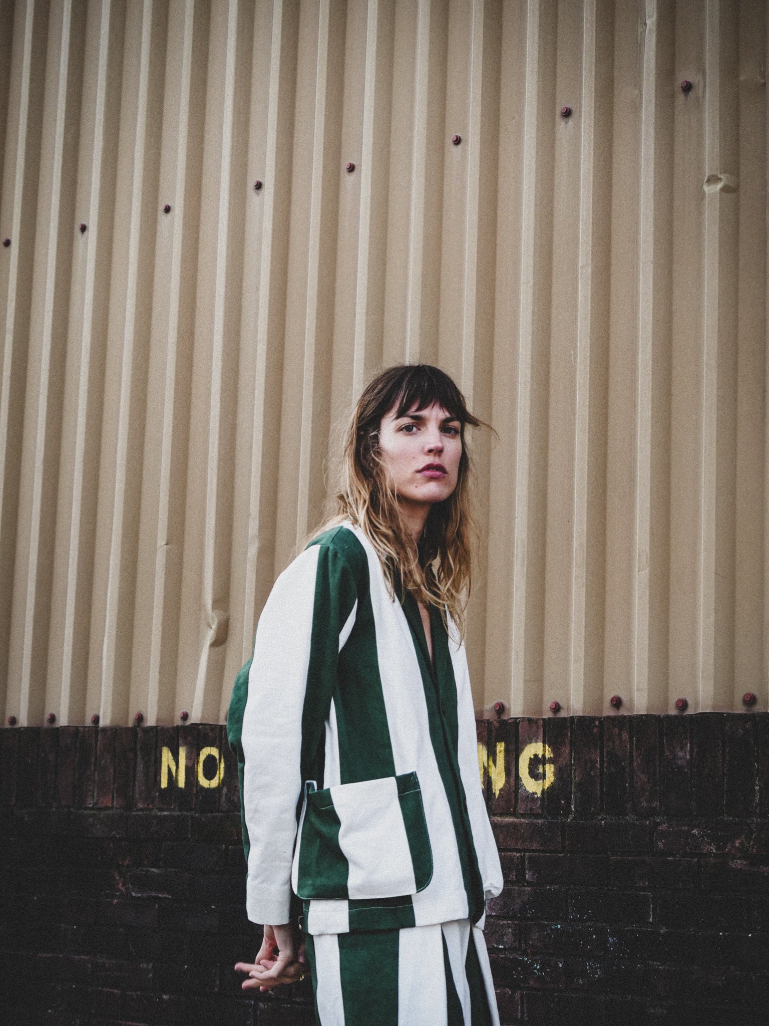 Woman wearing a green and white outfit standing against a corrugated metal wall.