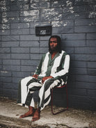 Person wearing a striped outfit sitting against a textured wall with a 'Post' box.