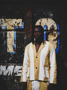 Person wearing a mustard and white outfit standing in front of a textured wall with large letters.