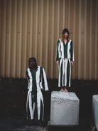 Man and woman wearing green and white outfits against a corrugated metal wall.