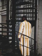 Person wearing a mustard and white striped outfit standing on a fire escape.