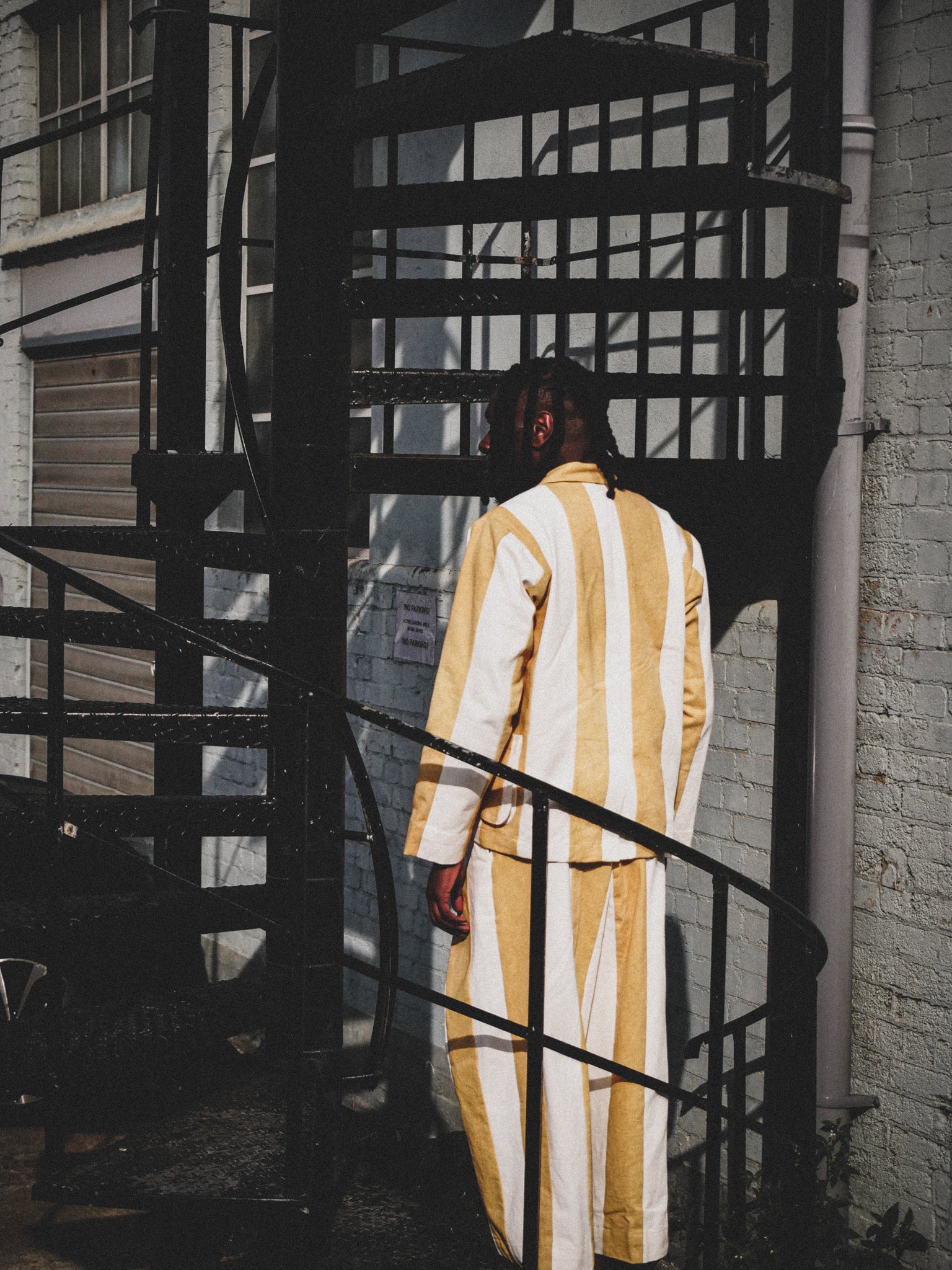 Person wearing a mustard and white striped outfit standing on a fire escape.