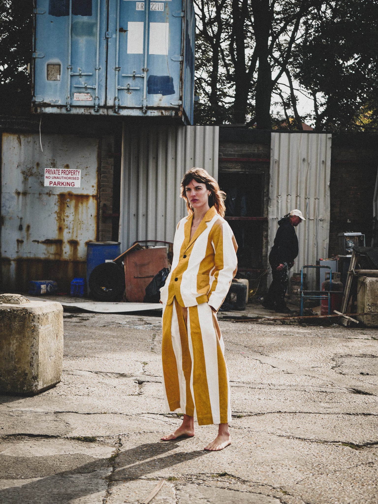 Person wearing a mustard and white striped outfit standing in an industrial area.