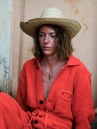 Woman wearing a red outfit and straw hat against a textured wall.