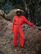 Man in sombrero wearing an orange jumpsuit and straw hat standing on a pile of hay with a natural background