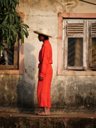 Man in sombrero in a red outfit standing against a weathered wall with a window.