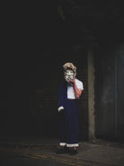 Person wearing a mask and blue outfit in a dark alleyway