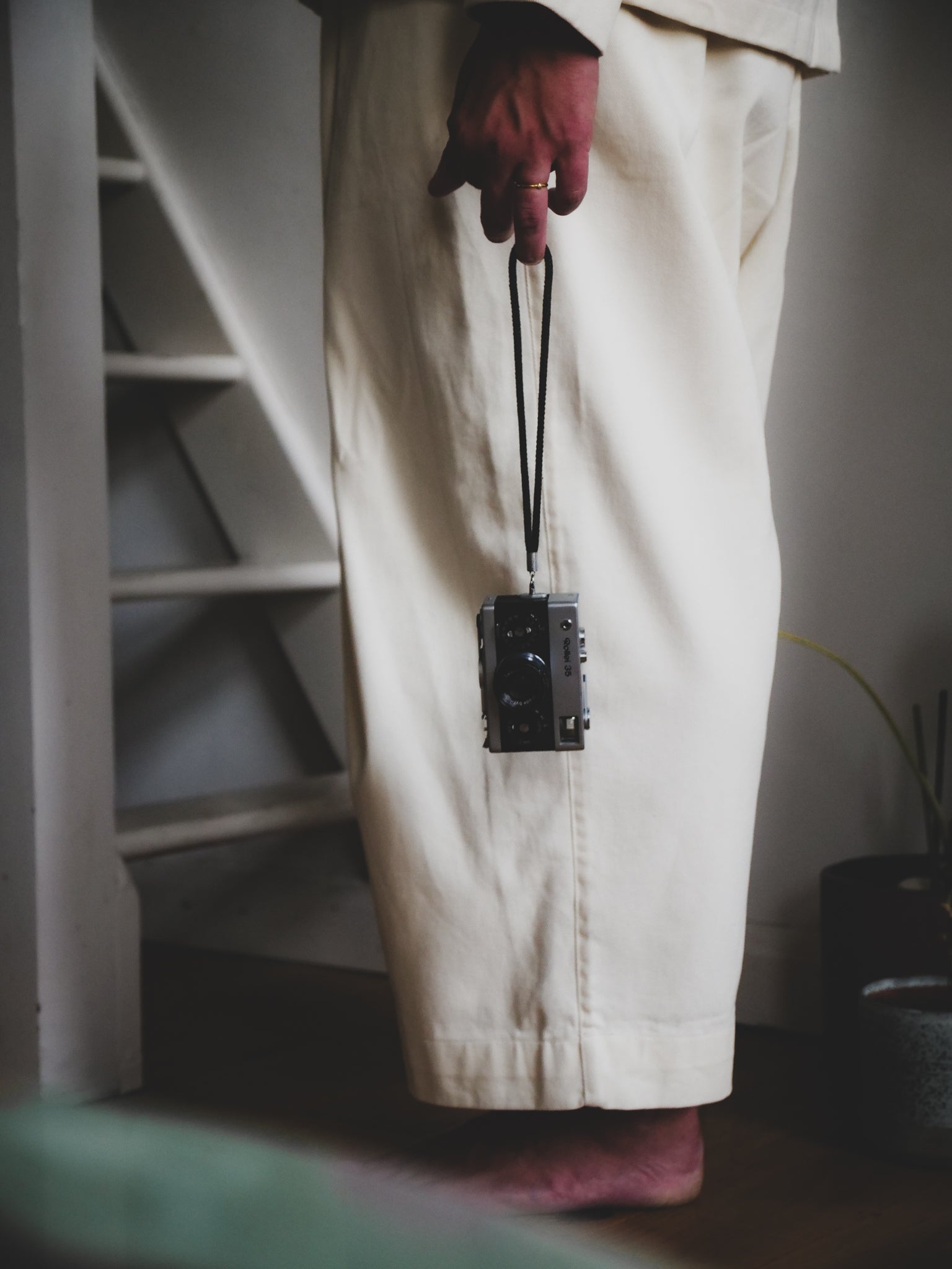 Person wearing beige pants and red gloves holding a black camera with a lanyard.