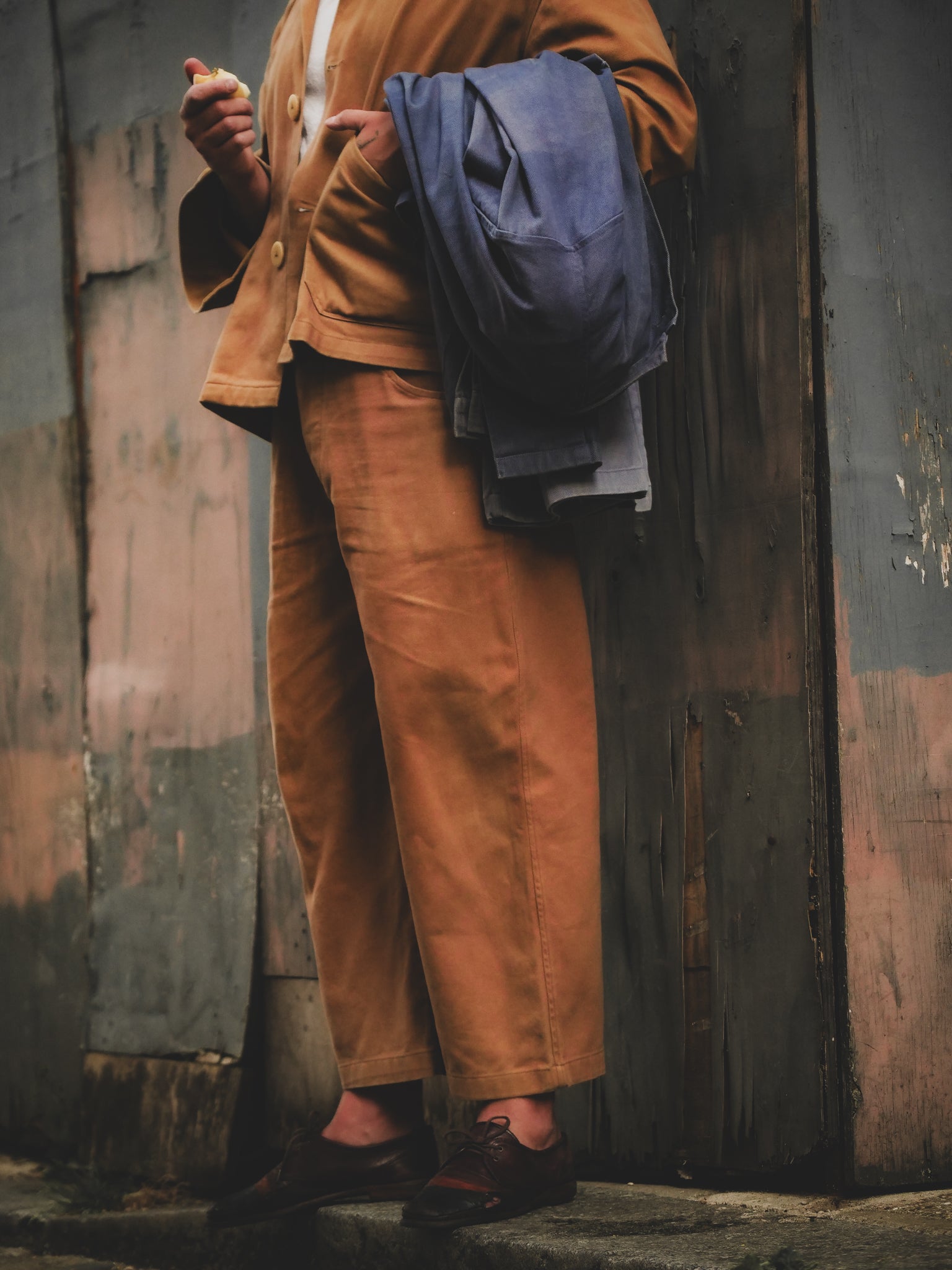 Person wearing a brown outfit holding blue fabric against a rustic wooden wall.