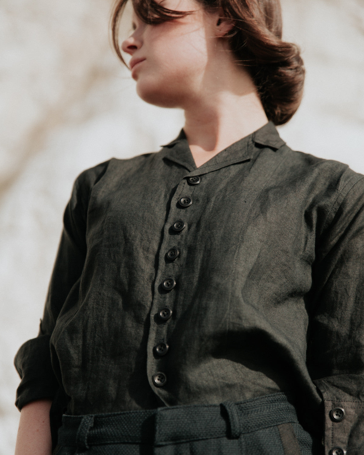 Person wearing a black shirt with buttons against a neutral background