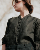 Person wearing a black shirt with buttons against a neutral background